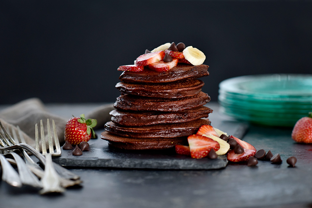 Gluten-Free Chocolate Banana Pancakes in a stack with strawberries and bananas